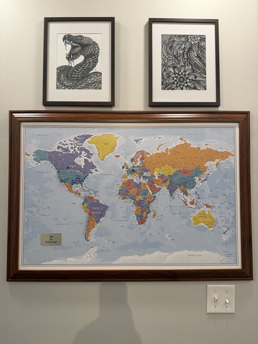 A world map hangs below two framed black-and-white prints of a cobra and floral design, with a small label reading "Our New World" in the corner—visually reinforcing the caption's message that "we are all here somewhere" on the shared map of the world.