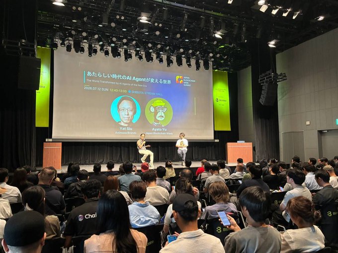 A fireside chat at the Japan Blockchain Week Summit (July 12, 2026, 12:40–13:00) features Ayato Yu of Japan Blockchain Week in conversation with Yet Siu, co-founder and executive chairman of World (Worldcoin), as shown on the large screen titled "The World Transformed by a Genesis of Era Phase 2: あらたしい時代のAI Agentが変える世界," with an attentive audience seated in the auditorium.