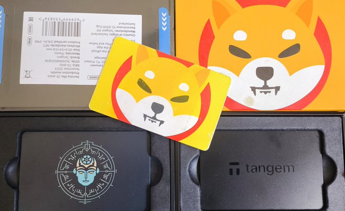A flat lay of Tangem crypto wallet packaging featuring Shiba Inu (SHIB) themed cards, including one with the iconic dog logo and another with a samurai helmet design.