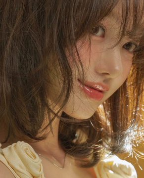 A close-up portrait of a young woman with soft, wavy brown hair and glossy lips, styled makeup enhancing her natural features as she gazes softly at the camera, perfectly matching the caption's description of captivating beauty.