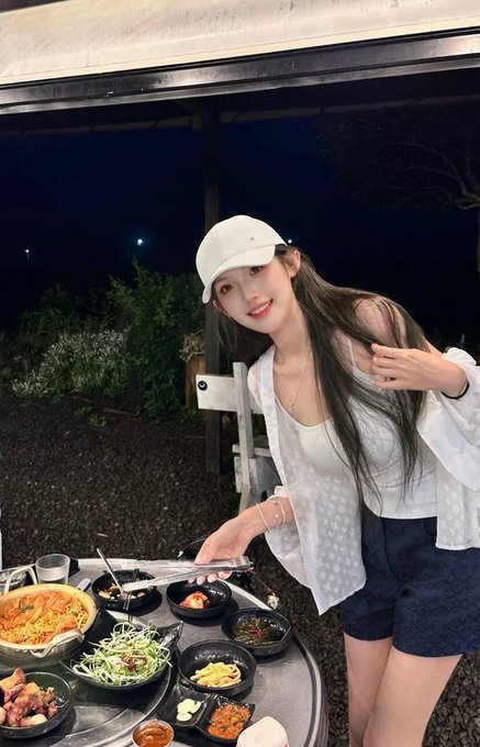 A young woman in a white baseball cap and open-shouldered top is preparing a Korean barbecue spread. The image aligns with the post's narrative about crypto airdrops being used as disguised promotional spending by project teams.