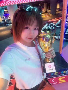 A selfie of a young woman wearing a white t-shirt and sunglasses on her head, holding a golden trophy with a 'Moxy' branded plaque, taken in what appears to be a Sony-themed entertainment venue.
