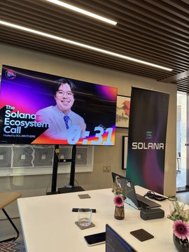A conference room with a screen displaying 'The Solana Ecosystem Call' alongside the Solana logo on the wall.