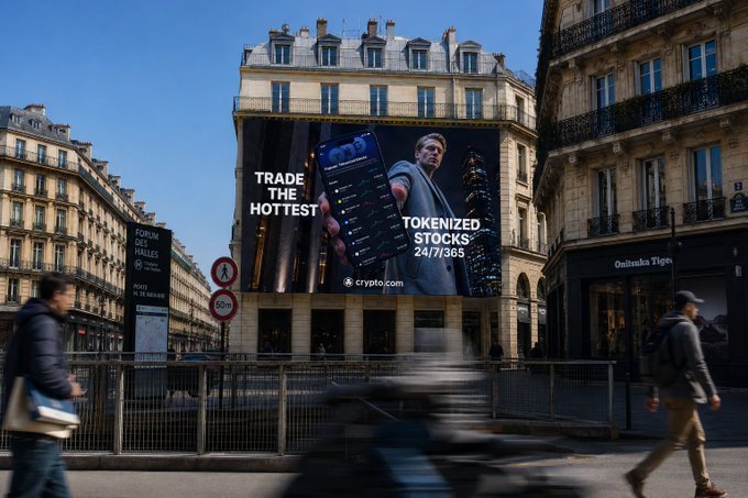 A large Crypto.com billboard on a Parisian building advertises "TRADE THE HOTTEST TOKENIZED STOCKS 24/7/365," promoting the platform's new round-the-clock trading feature for EEA users seeking U.S. asset exposure at any time.