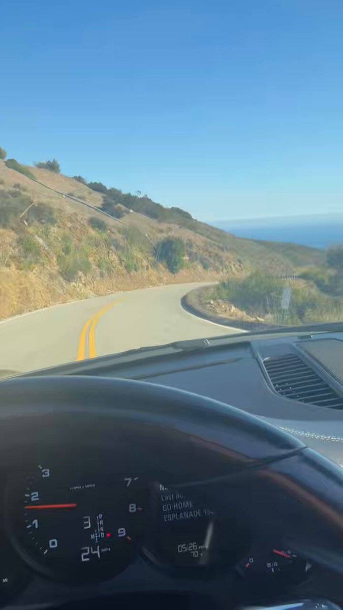 "Malibu up by" is a popular phrase used as a hashtag or a reference for a specific location, often associated with Malibu, California. In this case, the image captures the view from inside a car driving along a curvy road in Malibu, California. The sky above them is clear and blue, providing a beautiful backdrop to their journey.