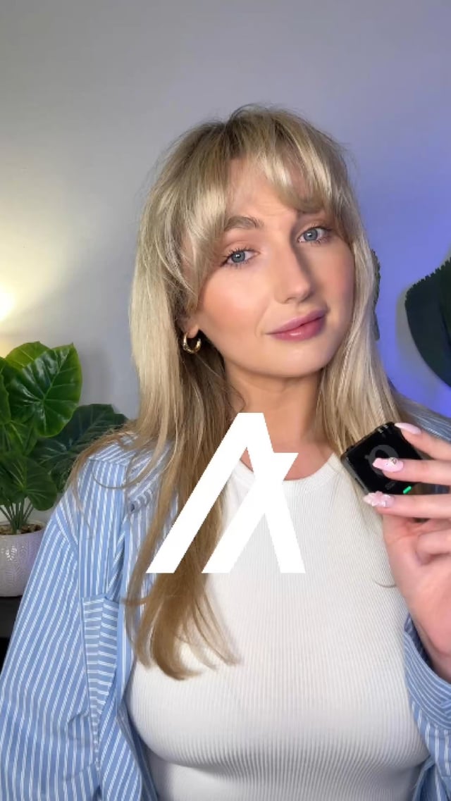A blonde woman with bangs in a blue striped shirt and white top holds a smartphone, with a large white stylized "A" logo overlaid on the image.