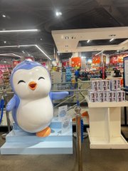 A penguin mascot figure stands in what appears to be a retail store or mall setting.