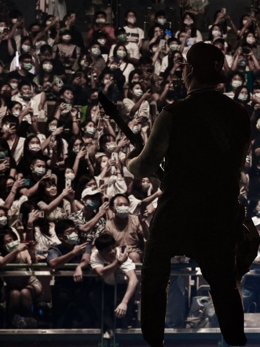 A silhouette of a guitarist performing on stage in front of a large crowd of masked fans holding up phones to record the concert.