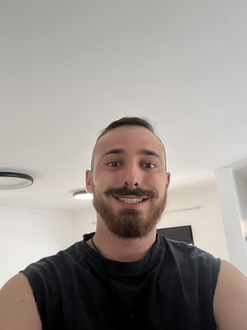 iced coffee with a mustache and beard, wearing black t-shirt and white wall backdrop.