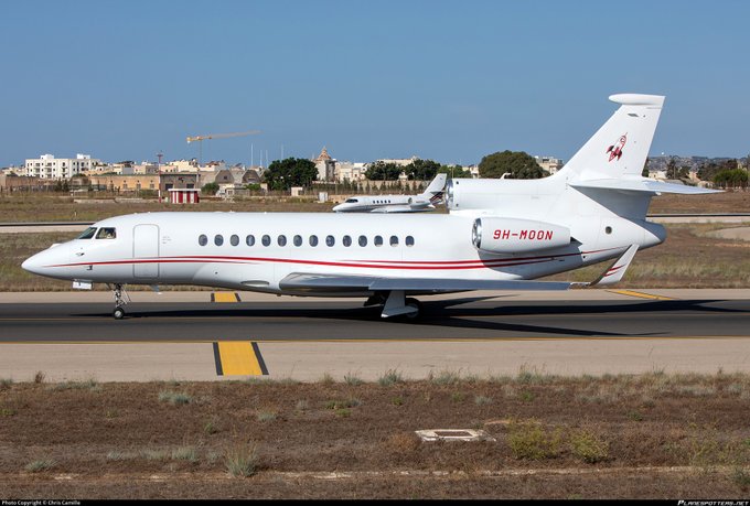 A white private jet with the registration '9H-MOON' and a red logo on its tail, taxiing on a runway.