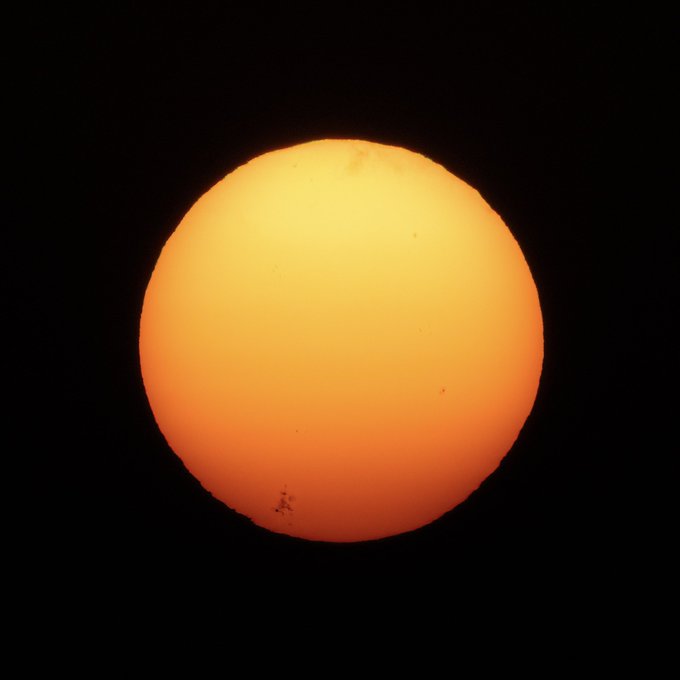 A bright orange-yellow sun is captured against a pitch-black sky, appearing to be photographed during an eclipse or sunset with a notably vivid, saturated glow.