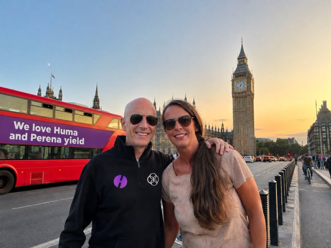 A smiling couple poses in front of London's iconic Big Ben and a red double-decker bus displaying an advertisement that reads "We love Huma and Perena yield," playfully echoing the post's message of weekend well-wishes and brand enthusiasm.