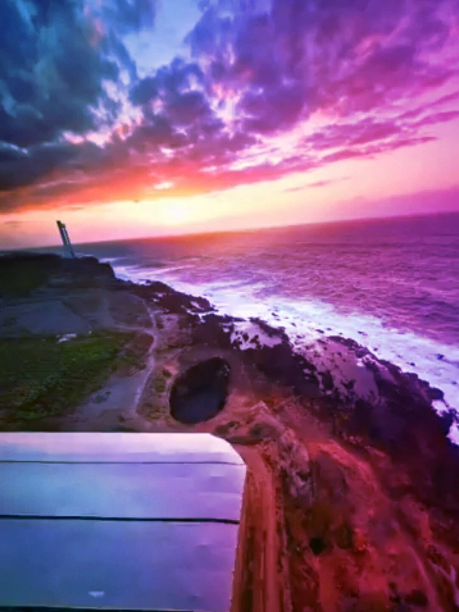 The image features a beautiful sunset over the ocean, with the sky painted in shades of purple and pink. The sun is setting behind the water, creating a stunning backdrop for the scene. In the foreground, there's an airplane wing visible on the left side of the photo. The text "gmonad to all the optimists and Monad believers hope you have a nice weekend" adds a touch of humor to the image, suggesting that even though the sky is darkening, it still brings joy and positivity to those who appreciate its beauty.