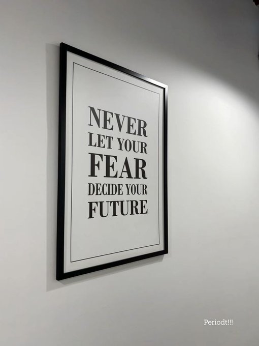 A framed poster on a white wall displays the motivational quote 'NEVER LET YOUR FEAR DECIDE YOUR FUTURE' in black text, with 'Periodt!!!' written below the frame.