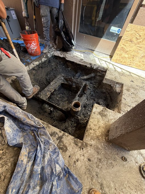 Workers remove a heavily deteriorated, grease-clogged old grease trap from an excavated pit outside a building, preparing the site for a brand-new installation. The grimy tank and surrounding mud reinforce the post's "Dirty Hands Clean Money" theme of tackling tough, profitable service work.