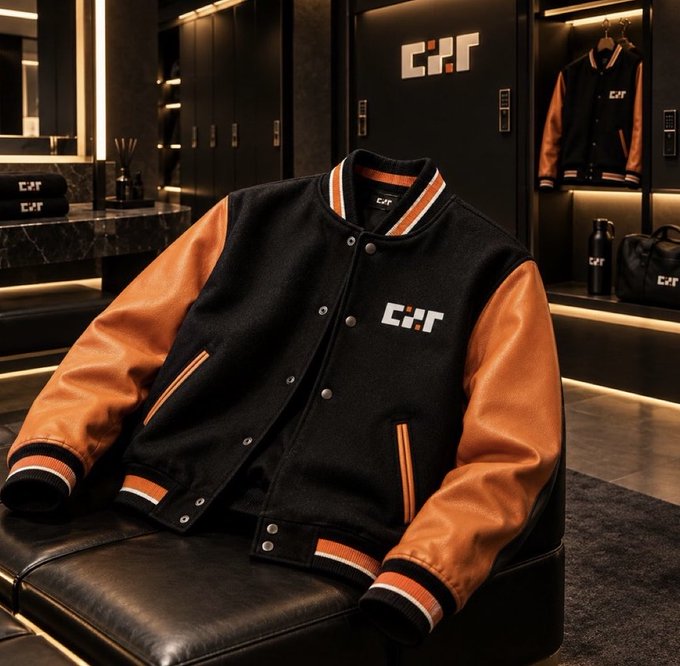 A black and orange varsity-style jacket with 'C:F' lettering displayed on a leather seat in a modern showroom setting.