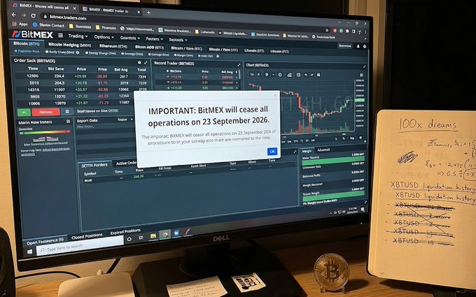 A desk setup showing a computer monitor displaying the BitMEX trading platform with a pop-up message stating 'IMPORTANT: BitMEX will cease all operations on 23 September 2026', alongside a notebook titled '100x dreams' with handwritten trading notes for XBTUSD.
