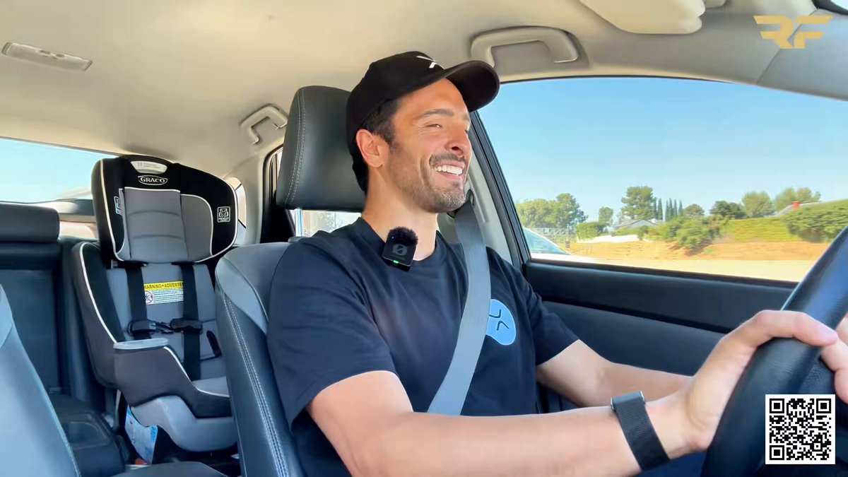 The image shows a man sitting inside a car, smiling as he drives down the road. The man appears to be wearing a black shirt and a baseball cap while driving his vehicle. There are also some text elements in the image that read "Self-custody is officially everywhere! @Tangem hardware wallets are FLYING off shelves at Best Buy, and I even took mine from So Cal straight to El Salvador aka #XRPFamily #Ad". The man's smile suggests he is enjoying his drive or possibly sharing a humorous moment with the text.