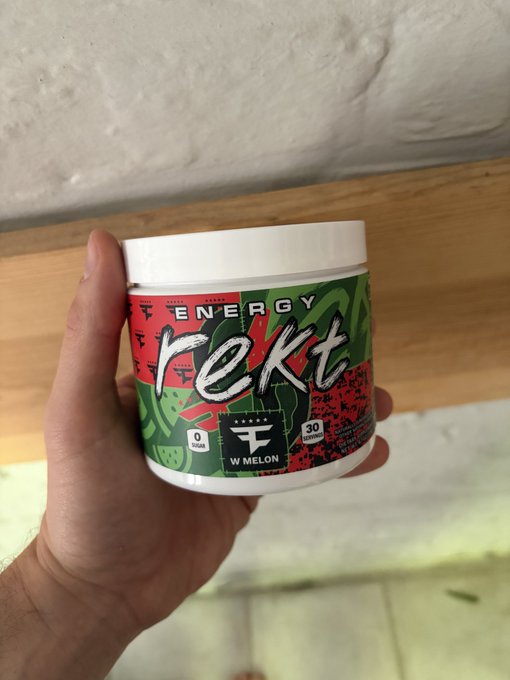 A hand holds a white tub of "REKT ENERGY" x FaZe Esports watermelon-flavored energy powder, displaying "0 SUGAR" and "30 SERVINGS" on the label. The product matches the post highlighting the collaboration between Rekt Drinks and FaZe Esports as a prime day delivery favorite.