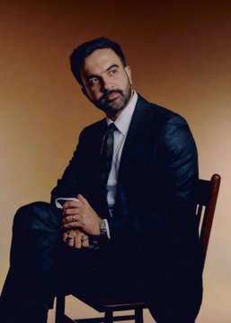 Zohran Mamdani sits in a dark suit and tie, gazing seriously toward the camera against a warm-toned backdrop. The portrait accompanies news that the New York City politician has surged ahead of Donald Trump in TIME's Person of the Year odds, now leading with a 22% chance of taking the title.