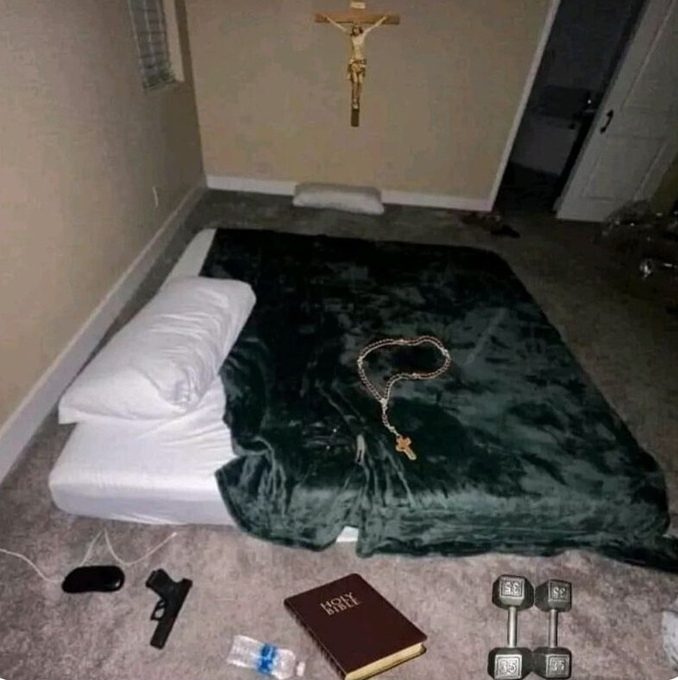 A humble bedroom floor mattress setup featuring a green blanket, white pillow, a crucifix on the wall, a "Holy Bible," and a handgun laid out beside it, mocking the stereotype that crypto-millionaires prioritize flashy lifestyles over faith and modesty. The juxtaposition of the pistol, Bible, and makeshift bed visually reinforces the joke about staying grounded—and possibly paranoid—even after striking it rich in crypto.