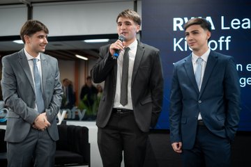 Three men in business suits at an RWTH Aachen Kickoff event, with one holding a microphone.