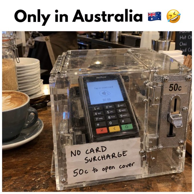 The image is captioned 'Only in Australia' and shows a Verifone card payment terminal inside a clear acrylic lockbox at a cafe, with a handwritten sign reading 'NO CARD SURCHARGE 50c to open cover' and a coin slot marked '50c'.