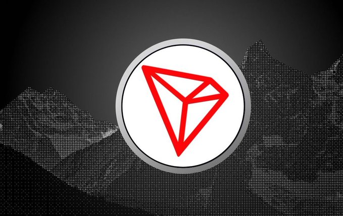 A red triangular logo inside a white circle displayed over a dark, textured mountain background, resembling the Tron (TRX) cryptocurrency symbol.