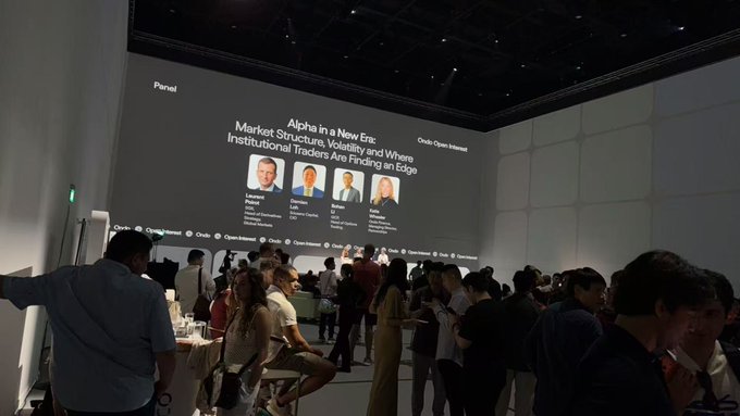 A networking event titled "Alpha in a New Era: Market Structure, Volatility and Where Institutional Traders Are Finding an Edge," hosted by Ondo, draws a large crowd of attendees despite the warm Singapore weather, with panelists Bernard (Baringa), Damien (JPMorgan), EJ (Block Scholes), and Mike featured on screen as the audience listens attentively.