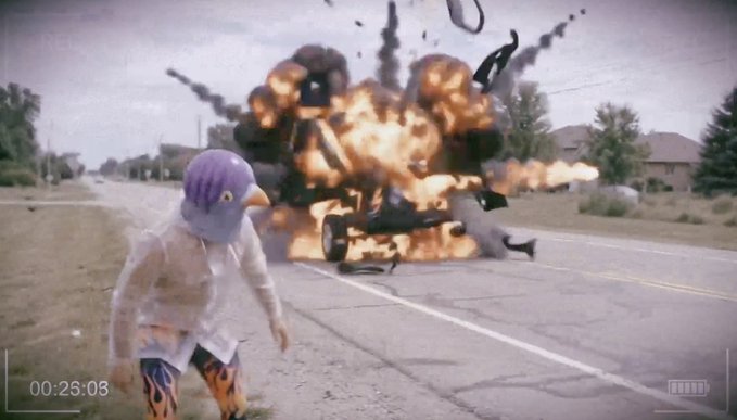 A surreal video still showing a person wearing a large purple bird mask running down a road while a car explodes behind them, with a timestamp of 00:25:08.