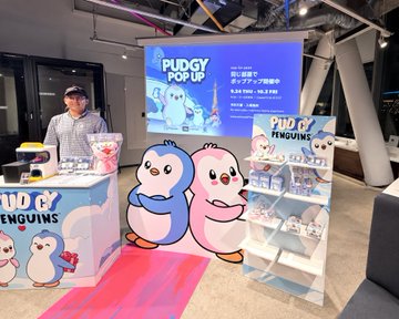 A "PUDGY POP-UP" promotional booth features large cutouts of two cute penguin characters from the Pudgy Penguins NFT collection, with a digital screen displaying event details including dates "9.26 FRI - 10.24 FRI" and times "11:00-19:00," while a staff member stands ready behind a counter of merchandise—aligning with the post's call to bring such a Pudgy Penguins pop-up experience to Canada.