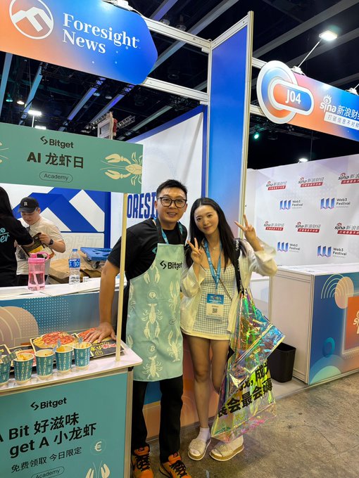 The image shows two people posing with peace signs at a Bitget booth featuring an "AI 龙虾日 Academy" promotion at what appears to be a Web3 Festival event. The accompanying post about "Learning the Bear Market Survival Guide" aligns with the crypto exchange setting shown, suggesting this was a Bitget-sponsored educational event during a crypto industry conference.