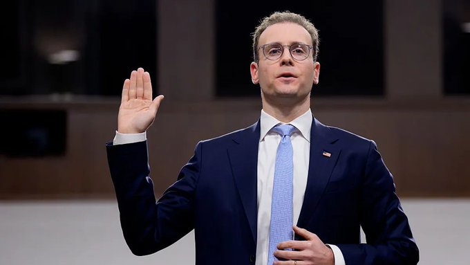 A man in a dark suit and blue tie being sworn in, raising his right hand in what appears to be a Senate hearing.