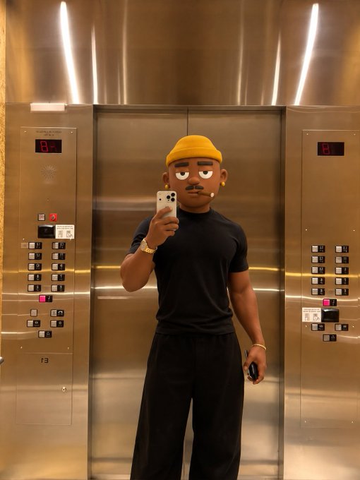A man wearing a yellow beanie, black t-shirt, and a cartoon face filter takes a mirror selfie with his phone inside an elevator.