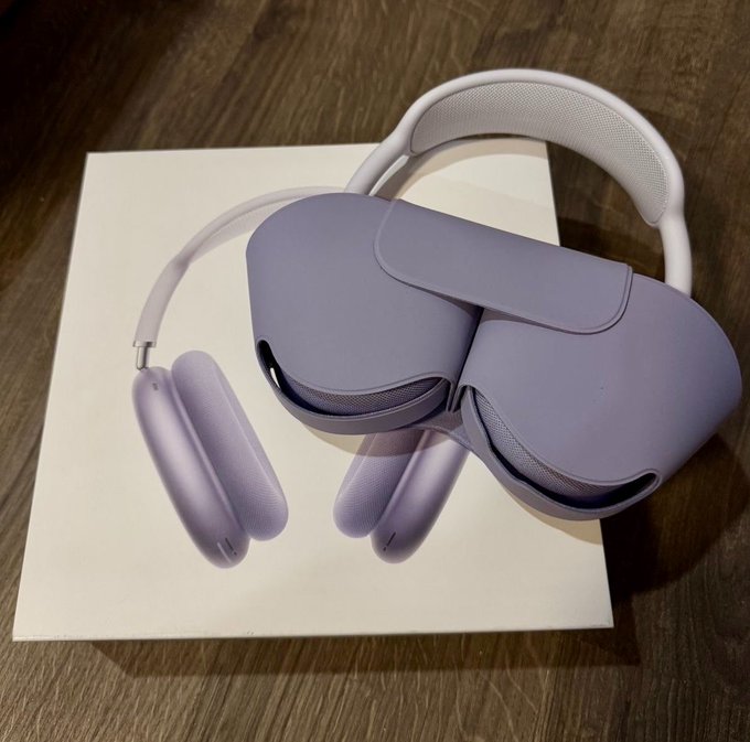 A photograph of purple/lilac Apple AirPods Max headphones resting on top of a white box on a wooden surface.