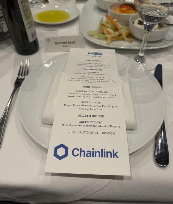 A printed event menu rests on a table setting with the Chainlink logo, listing courses including Calamari, Loup de Mer, and Filet Mignon.