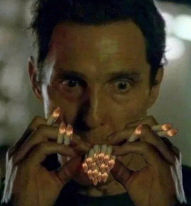 A close-up still of actor Steve Buscemi holding a cluster of lit cigarettes, appearing startled with wide eyes.