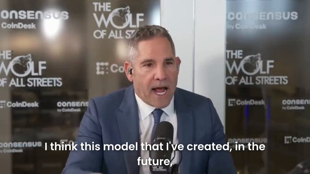 The image features a man wearing a suit and tie sitting at a desk with a microphone in front of him. The background shows a sign that says "consensus" and "coinDesk", as well as an advertisement for "The Wolf of All Streets".