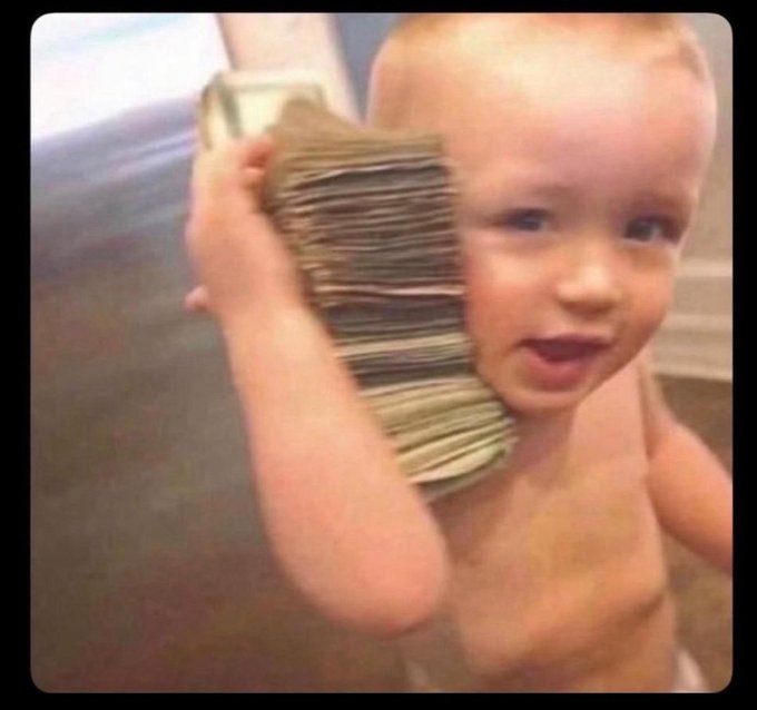A humorous photo of a smiling shirtless toddler holding a thick stack of cash next to their face.