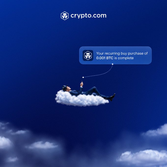 A businessman relaxes on a cloud wearing a VR headset beneath the Crypto.com logo, with a notification bubble reading "Your recurring buy purchase of 0.001 BTC is complete"—visually capturing the post's message of hands-free, on-autopilot crypto investing with the Recurring Buy feature.