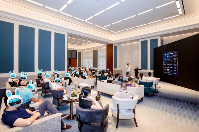 A gathering of people sits in a modern, elegant lounge area, with several faces covered by cartoon rabbit emojis.
