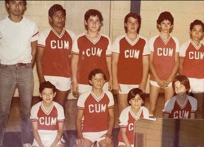 A vintage team photograph showing a group of boys and one adult man, all wearing matching red and white jerseys with 'CUM' printed across the chest, arranged in standing and kneeling rows.