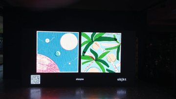 The image features an exhibition with two large screens displaying different artwork, one depicting a tropical scene with palm trees and the other showcasing a space-themed painting of planets. The artworks are displayed side by side, allowing viewers to compare and contrast the artistic styles and themes presented in each piece.