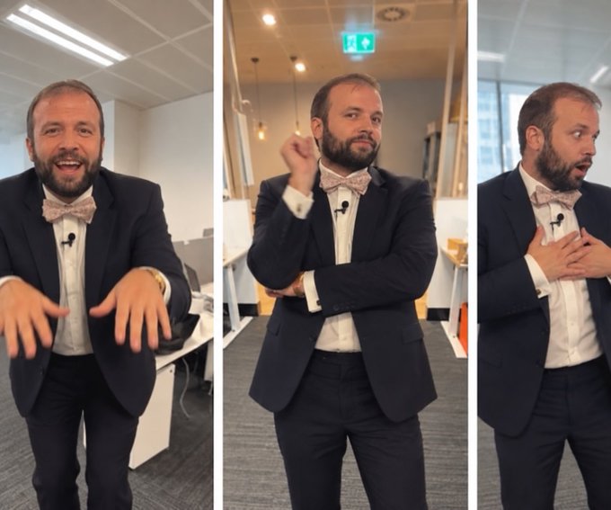 A man in a navy suit and pink bowtie gestures expressively across three panels in an office setting, with an emergency exit sign visible in the middle frame. His animated expressions and hand movements humorously reference the "Gaming L1 and a hairline" caption, playfully emphasizing his receding hairline while engaging with an audience.