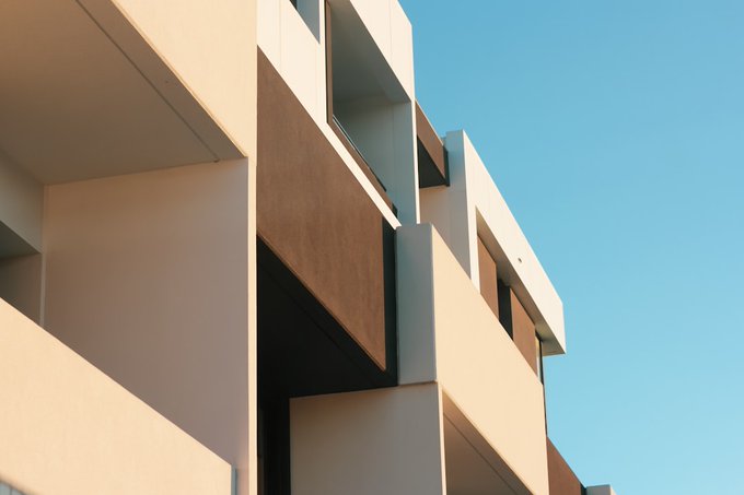 An architectural photograph showing the geometric, modern facade of a building with beige and brown panels against a clear blue sky.