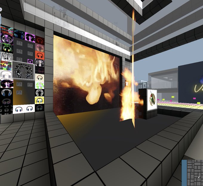 A blocky, video game-style environment features a large wall-mounted screen displaying a fire animation, with an actual fire effect bursting upward from a small machine on the tiled floor nearby.