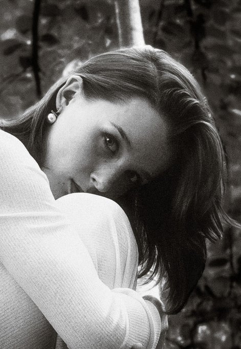 A black and white portrait of a young woman with long hair, wearing a white sweater and a small earring, rests her chin on her arm with a contemplative expression, embodying the introspective and artistic mood of the pencil art promotion featuring a quote about wild spirit, soft heart, and sweet soul.