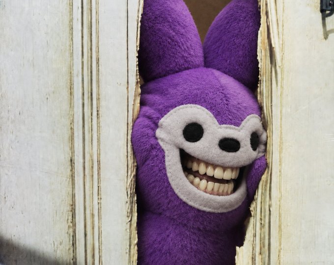 A purple plush toy with a creepy wide grin and prominent human-like teeth peers through a narrow gap in a weathered white door.