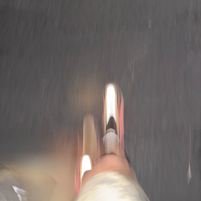 Blurry, motion-streaked photo of feet in sneakers walking or running on a dark pavement surface.