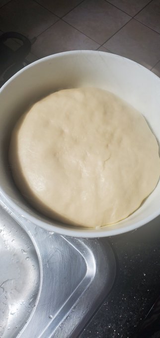 A bowl of smooth, risen dough sits on a stainless steel sink, having been left to proof or rise.